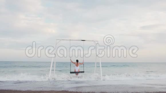快乐的年轻女子穿着白色泳衣骑在秋千上享受海景假期概念视频的预览图