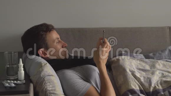 一个不健康的男人躺在床上在他家的药物旁边打电话感染感冒和冬季流感病毒的人视频的预览图