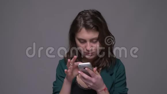 为一位深褐色头发的成年女性拍摄的特写镜头她在手机上发短信看着镜头带着背景微笑视频的预览图