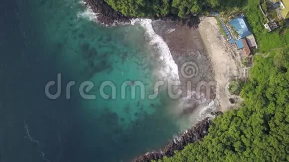 鸟瞰狭窄的黑色火山沙滩被印度尼西亚丛林包围的小型海洋胜地视频的预览图
