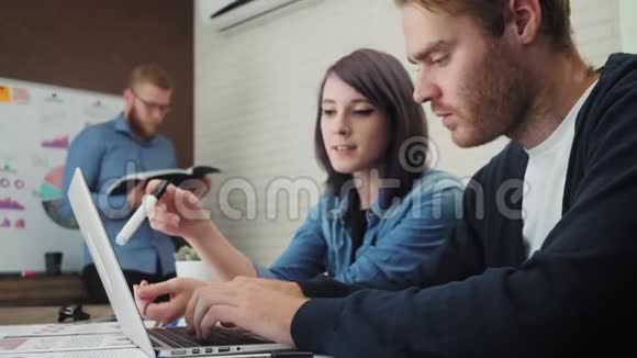 一群年轻的商人在办公桌前工作和交流看着笔记本电脑视频的预览图