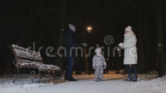 一对年轻夫妇在傍晚的冬季公园里向一个小女儿泼雪视频的预览图