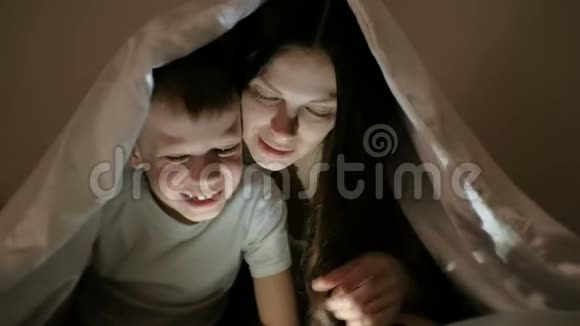 年轻女子妈妈和儿子一起在平板电脑上看一部有趣的电影在毯子下面笑视频的预览图