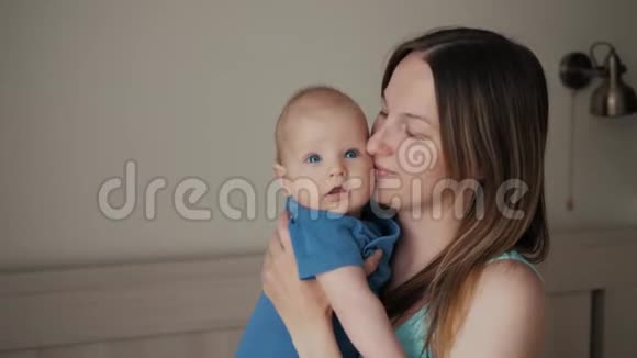 年轻的母亲抱着她的新生儿熟睡的孩子家里的家人卧室里的妈妈和小男孩亲吻她视频的预览图