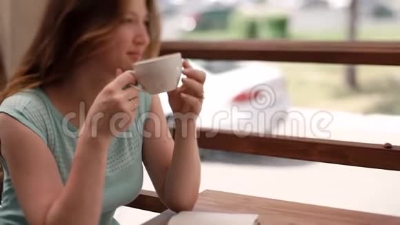 一个穿蓝色连衣裙的女孩正在夏天的咖啡馆里喝咖啡视频的预览图