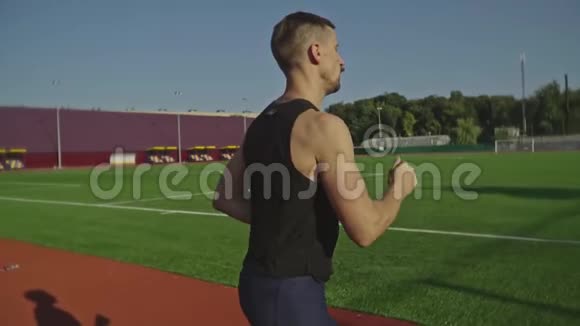 一个留胡子的运动员沿着绿色足球场附近的跑道跑慢动作射击视频的预览图