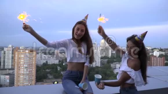 慢镜头拍摄两个快乐的黑发吹口哨在明亮的帽子和庆祝生日快乐的屋顶上视频的预览图