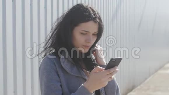 年轻女性在街上使用智能手机的肖像风很容易吹动她的头发视频的预览图