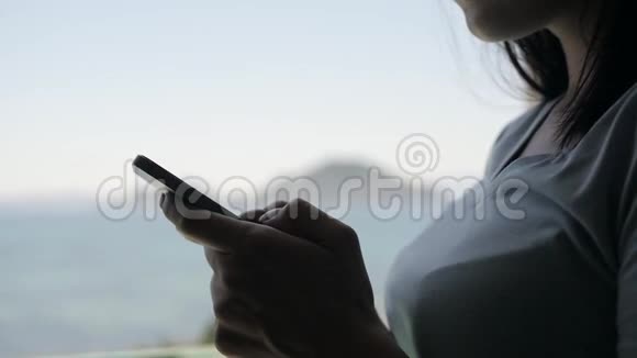 使用智能手机的年轻女性肖像高加索模特站在窗口用她的智能手机视频的预览图
