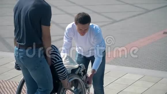 两个男人在台阶上举起一个坐轮椅的女人坐轮椅的年轻女子和两个男人在户外视频的预览图