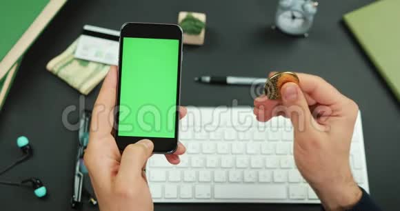 男人拿着一部黑色智能手机绿色屏幕覆盖着一张工作桌和一个金色的比特币视频的预览图