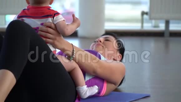 当妈妈在瑜伽垫上抽压时当她的小宝宝坐在肚子上时慢镜头拍摄视频的预览图