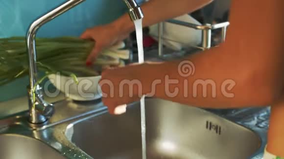 女人带着洋葱在水中洗涤站在水槽边视频的预览图