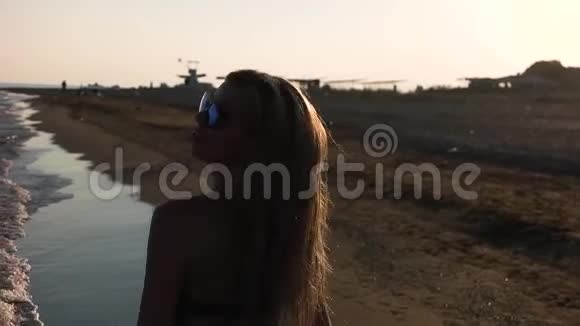 一个穿泳衣的女孩沿着海岸线散步视频的预览图