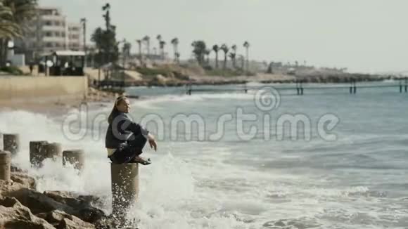 年轻女子坐在海边的柱子上视频的预览图