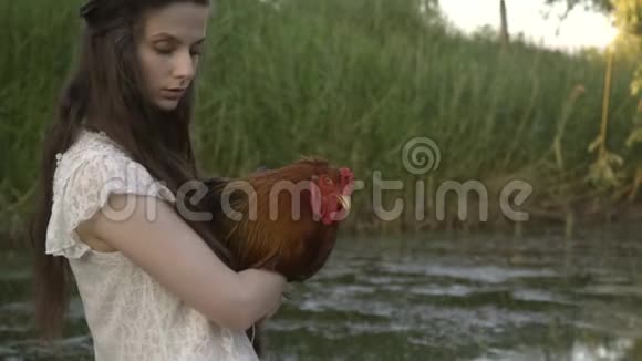 穿着白色衣服的农村女孩在河上抱着公鸡放松辙叉的生活视频的预览图
