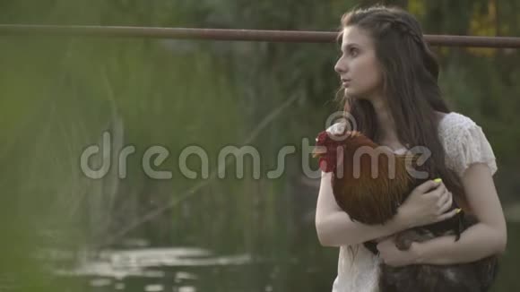 深褐色的女人坐在木桥上抱着一只公鸡放松生活视频的预览图