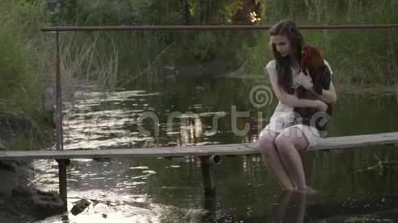 她穿着一身白色连衣裙体贴的黑发双脚在水里翻来覆去抱着坐在木桥上的公鸡视频的预览图