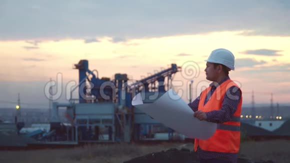 在公司背景下戴着头盔的工作工程师在日落时拿着一幅画视频的预览图