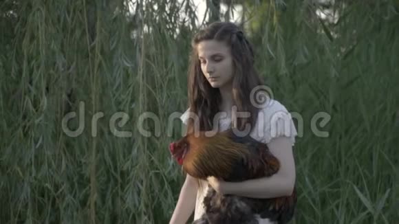 手里拿着公鸡的布鲁内特在柳树间奔跑乡村生活视频的预览图
