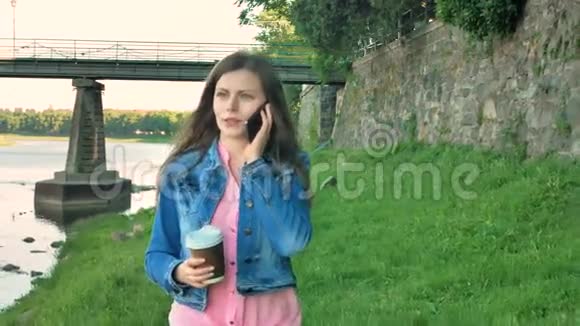 漂亮的年轻女孩走在海滨用智能手机聊天喝咖啡野桥和老墙视频的预览图