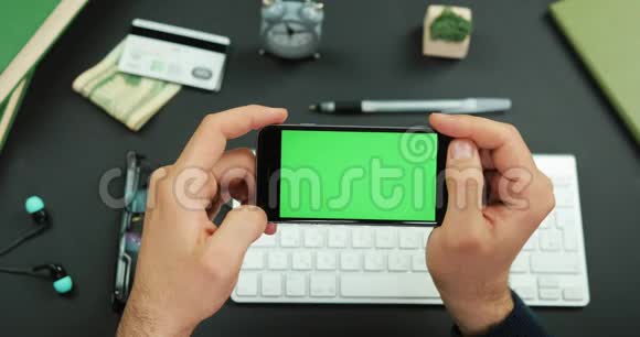 男人拿着一个绿色屏幕的黑色智能手机在工作桌上敲了敲它的东西视频的预览图