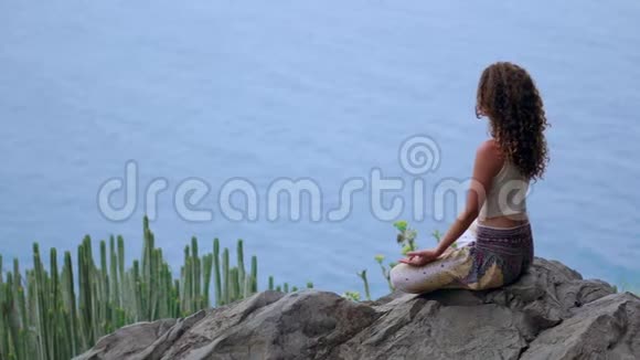 年轻女子在山上做瑜伽在一个岛屿上俯瞰大海坐在山顶的岩石上视频的预览图