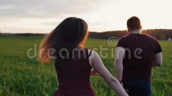 幸福的女人在日落时追逐她的男人在田野里奔跑女人的头发在风中摇摆后退慢点稳拍视频的预览图