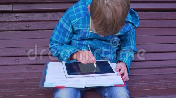 一个小学生在户外用课本和平板电脑做作业的画像视频的预览图