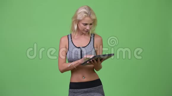 年轻快乐的美女一边思考一边用数码平板电脑准备健身房视频的预览图