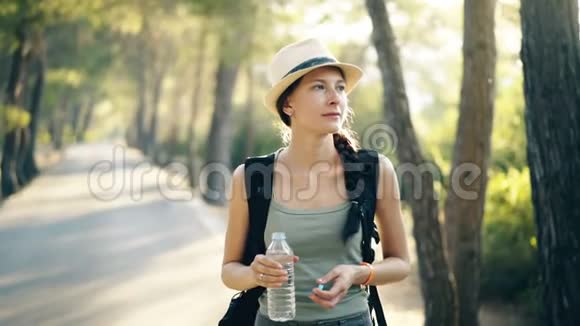 背包旅行后年轻迷人的旅游女孩喝水提神视频的预览图