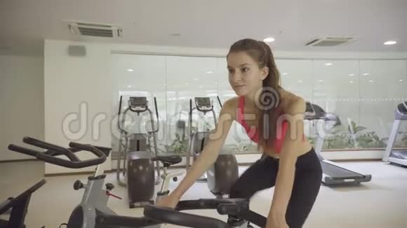 年轻女子在健身房骑自行车视频的预览图