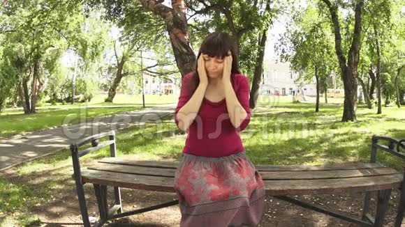 一个抑郁和头痛的女人坐在公园里抚摸威士忌视频的预览图