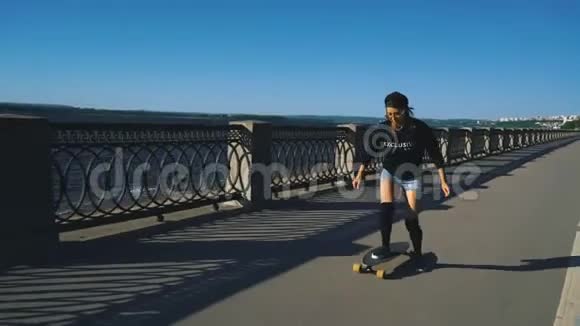 美丽的年轻女孩骑在他的长板上在靠近路堤的道路上极限运动视频的预览图