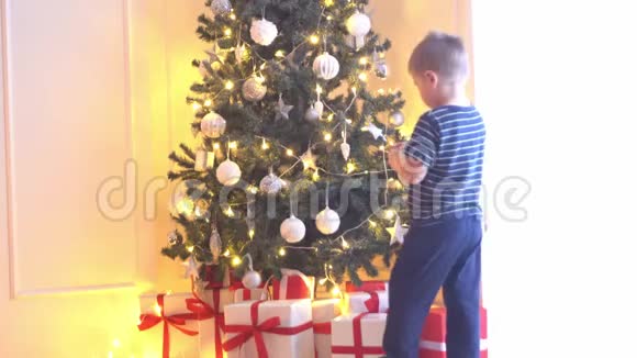 可爱的小男孩用球和灯装饰圣诞树在家里准备过年的孩子视频的预览图