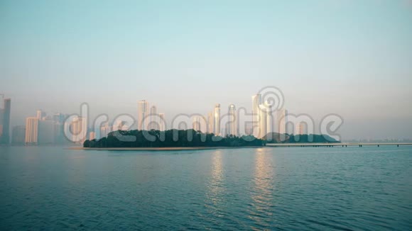 城市背景早晨城市景观与摩天大楼蓝天反映在蓝色海洋中的建筑物绿岛被锁定视频的预览图