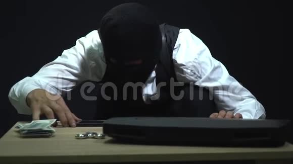 戴着面具的强盗正在检查一部智能手机一台笔记本电脑一捆美元带着一个旋转的人散步视频的预览图