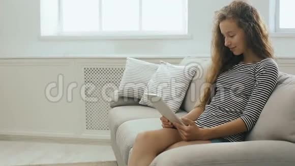 沙发上美丽的少女正从平板电脑上看书微笑着看着镜头视频的预览图