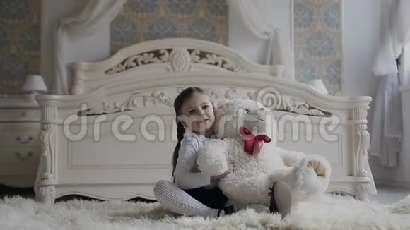 一个迷人的女孩坐在床边的地板上快乐地玩着柔软的泰迪熊快乐的宝宝和她的泰迪熊视频的预览图