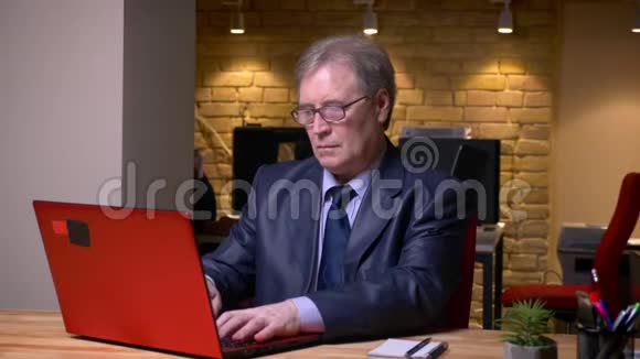 穿着正式服装的老人在办公室的笔记本电脑上打字的肖像视频的预览图