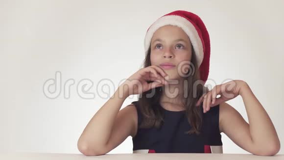 美丽的少女戴着圣诞老人的帽子梦想着礼物收到想要的礼物在白色背景下兴奋不已视频的预览图