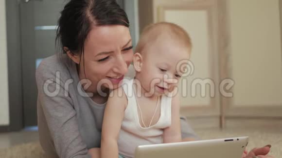 年轻的母亲和小男孩在地板上的地毯上玩平板电脑妈妈和儿子玩数字平板电脑视频的预览图