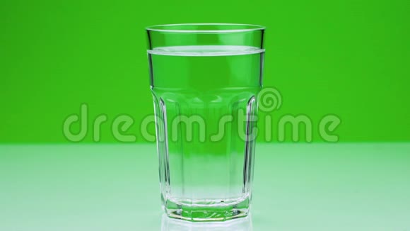 一片止痛的泡腾片落入玻璃杯中在一片绿色的阿司匹林上溶解特写慢镜头视频的预览图