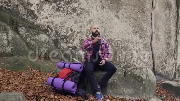 游客在一块岩石上休息靠近一座高崖从背包里拿出一杯热茶喝茶尽情享受视频的预览图