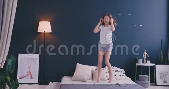 一个小女孩的肖像带着耳机听音乐在父母的床上跳舞概念音乐视频的预览图