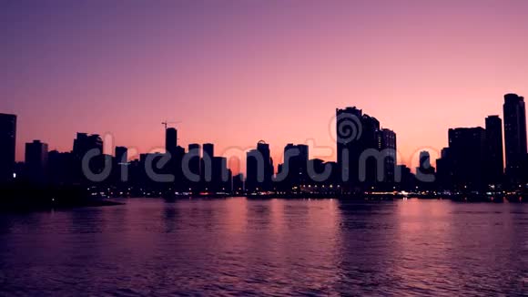紫色日落在美丽的泻湖与天际线湖和地平线上的摩天大楼大城市的夜景视频的预览图
