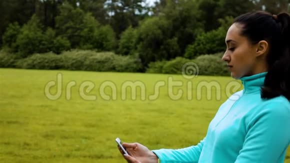 年轻女子慢跑者站在自然小径上用手机拍一张微笑的自拍视频的预览图