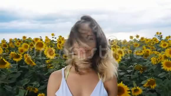 一位年轻女子在向日葵的田野上的肖像风吹着她的头发背景上的雷云视频的预览图