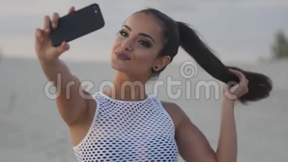 美丽的黑发女人在海滩上自拍夏天在海滩上的一位年轻女子在沙滩上拍照视频的预览图
