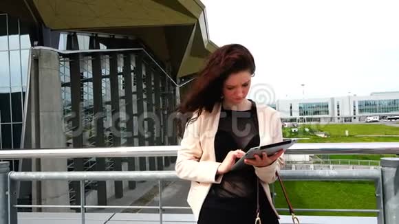 穿夹克的女人在建筑物优雅的建筑附近使用IT技术视频的预览图